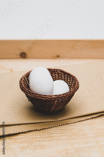 white eggs in a wicker canister on a wooden and brown paper background with text space