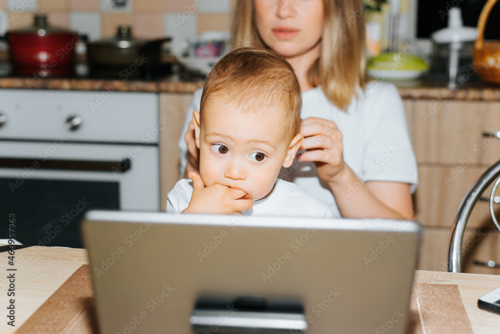 Motherhood, parenting, childcare. Mom and child using tablet, watching educational children's video. Baby boy sucking fingers and looking at display of gadget while sitting with mother, indoors Motherhood, parenting, childcare. Mom and child using tablet, watching educational children's video. Baby boy sucking fingers and looking at display of gadget while sitting with mother, indoors