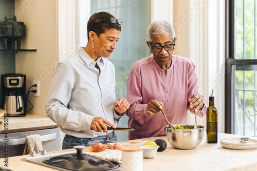 An adult woman and her senior mother make a meal together standing in the kitchen