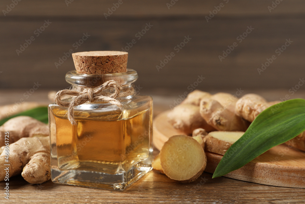 Glass bottle of essential oil and ginger root on wooden table Glass bottle of essential oil and ginger root on wooden table