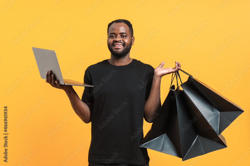 Black bearded man using laptop while posing with shopping bags