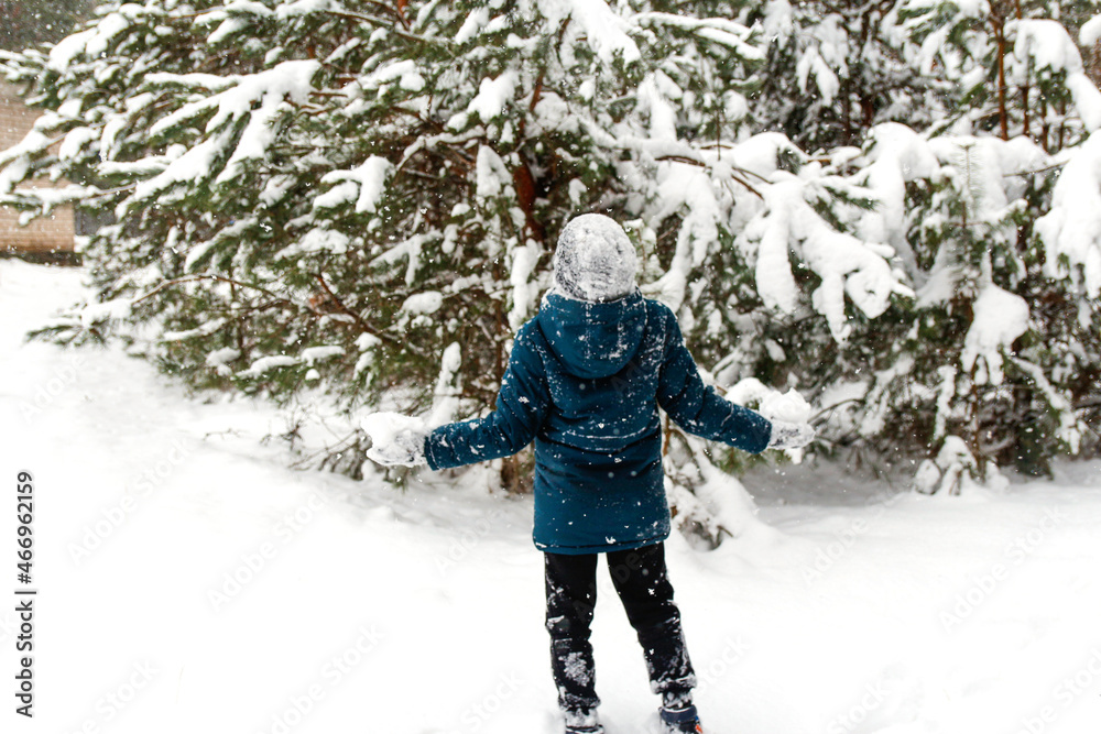 Back view of child boy in winter forest in snowstorm. Actively spending time outdoors. Winter snowy woodland. Cold frost weather in snowstorm. Happy childhood. Kid showing power