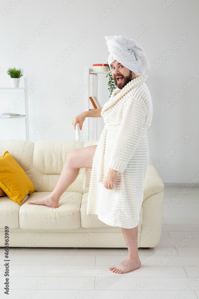 Funny portrait of handsome beautiful guy in towel and bathrobe holding tube of body cream lotion in hand. Spa, body and skin care for man concept Funny portrait of handsome beautiful guy in towel and bathrobe holding tube of body cream lotion in hand. Spa, body and skin care for man concept