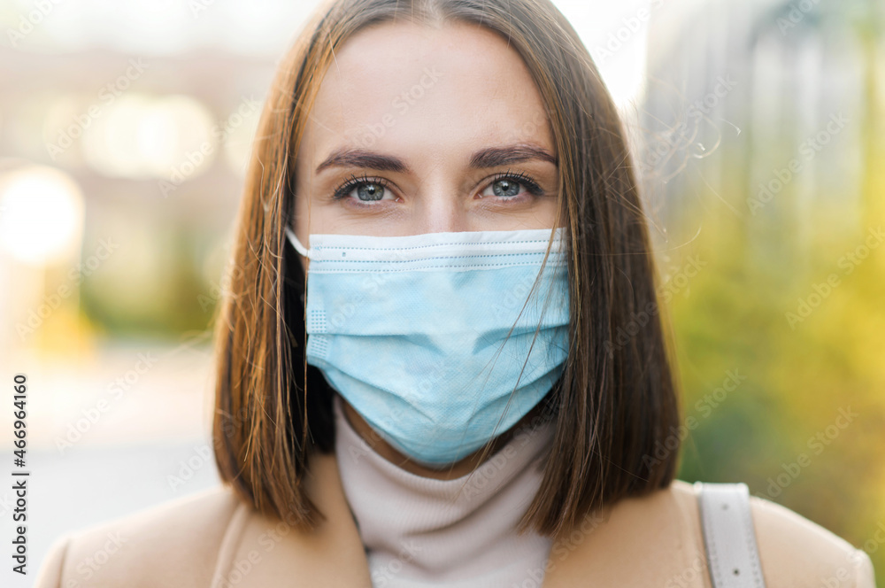 Close-up portrait of woman wearing protective medical mask looks at the camera. Protect yourself during a pandemic