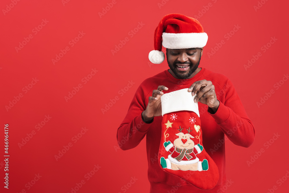 Black man wearing Santa hat smiling while looking in Christmas sock