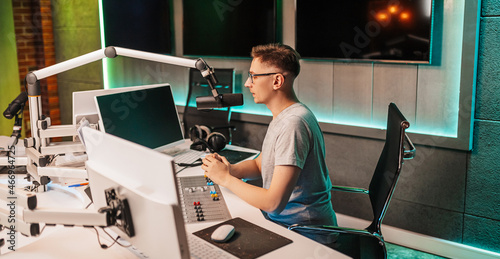 The DJ hosts the program and communicates with the audience on air at the radio station. The announcer reads the news. A male radio host speaks into a microphone and records a podcast photo