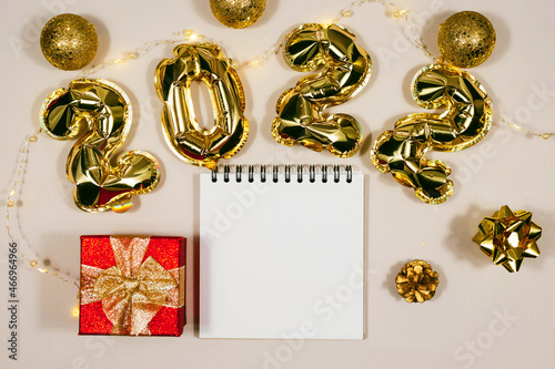 Golden 2022 balloons, gift, balls, notepad isolated on grey background. Helium balloons, gold foil numbers. Numbers for Happy New Year 2022. Party decoration, celebration, carnival.