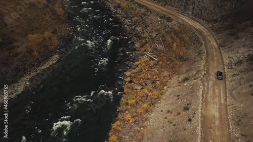 A black SUV jeep car is driving along an empty country road in the huge Katu-Yaryk canyon Chulyshman Valley with a large mountain bubbling river. Altai, Siberia, Russia. People travel along a dirt