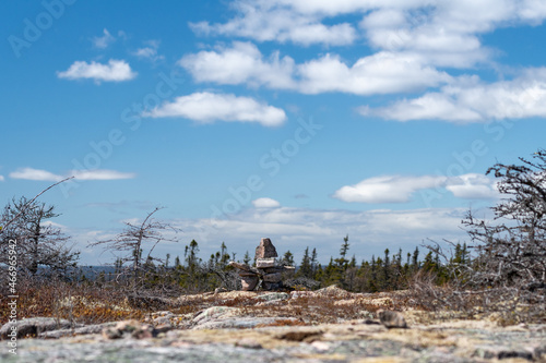 Inukshuk, a stack of granite rocks in the form of a person. The formation is a symbol of direction. The Inuit traditional figure is high on a hill. The background is a blue sky with some clouds. 