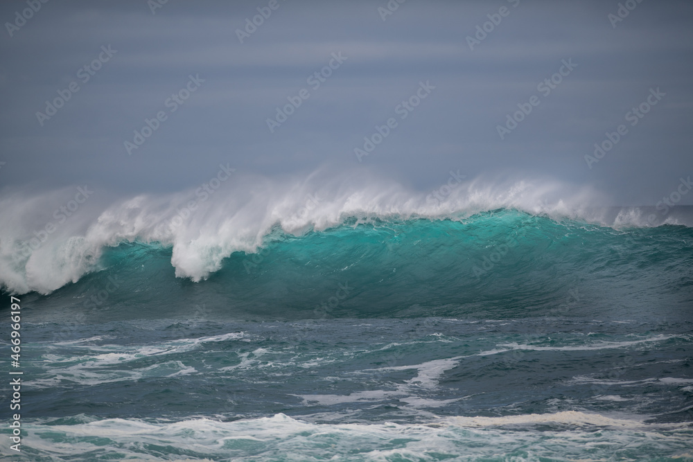 Obraz premium An angry turquoise green color massive rip curl of a wave as it rolls along the ocean. The white mist and froth from the wave are foamy and fluffy. The Atlantic Ocean in the background is deep blue