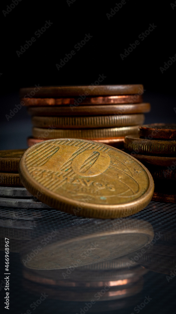 moedas empilhadas em superfície de vidro, refletindo no vidro, em um fundo escuro, com o foco em uma moeda de 10 centavos de BRL. moedas empilhadas em superfície de vidro, refletindo no vidro, em um fundo escuro, com o foco em uma moeda de 10 centavos de BRL.