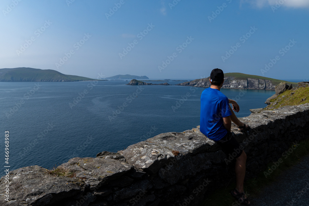 Young traveler man sitting on road looking at blue sea