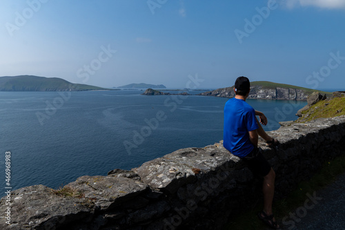 Young traveler man sitting on road looking at blue sea