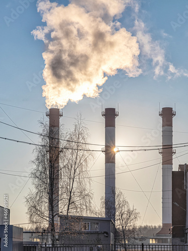 View against the sun on the smoking pipes of the thermal power plant photo