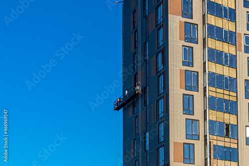 Workers in a construction cradle, doing their job on the facade of the building