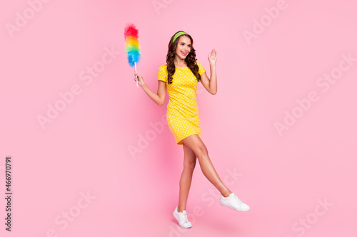 Photo of adorable funny young lady dressed dotted dress holding duster walking smiling isolated pink color background