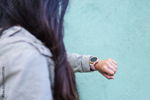young woman looking at the time on her smartwatch, arm detail, unrecognizable model, out of focus background, green background, selective focus