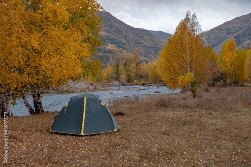 Green tent near river with colorful mountain forest in autumnseason. Autumn nature landscape. Tourism, trekking in fall season concept. Nature of Dzungarian Alatau in Kazakhstan.