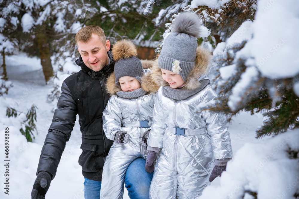 Portrait of playful happy family in winter snowy forest. Father and mother with two small children in winter nature, walking in the snow. Children in warm ski suits