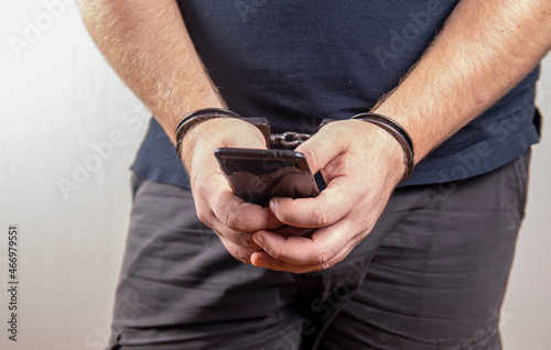 A man holding his phone in handcuffs on a white background,selective focus.Concept: the slave of technology, the right to one call, communication with a lawyer.