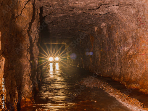 Fototapeta Naklejka Na Ścianę i Meble -  coming car lights from inside deep old mining tunnel cave with reflection. rock wall cave with water lodge rocky road. adventure travel in Thong Pha Phum, Kanchanaburi, Thailand called 3D tunnel.