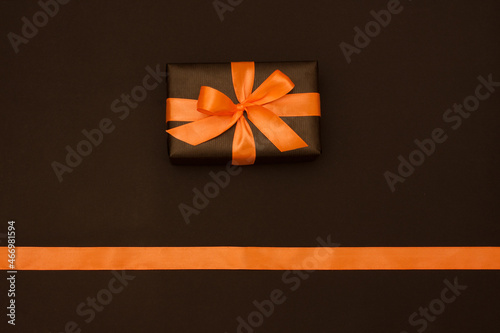 One rectangular gift box is packed in black paper, decorated with orange satin ribbon, on black background. Flat lay