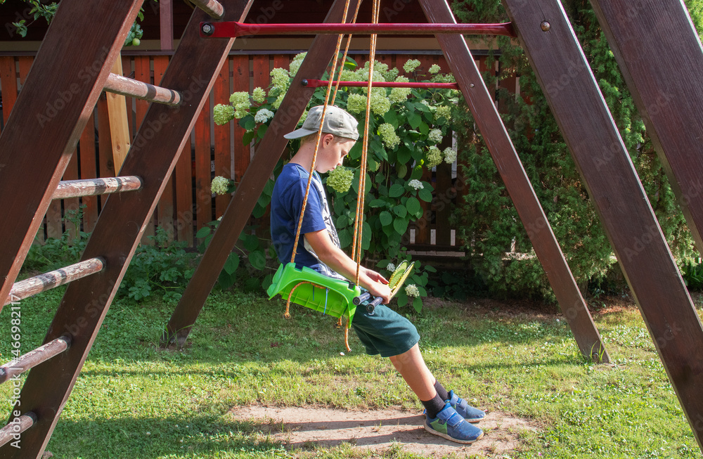 Fototapeta premium boy swinging on a swing in the summer village