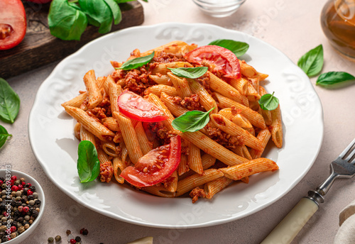 Penne pasta with tomato sauce and fresh tomatoes on a light background.