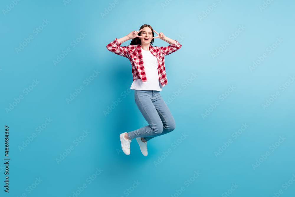 Full length photo of happy cheerful young woman make v-signs jump up smile isolated on blue color background