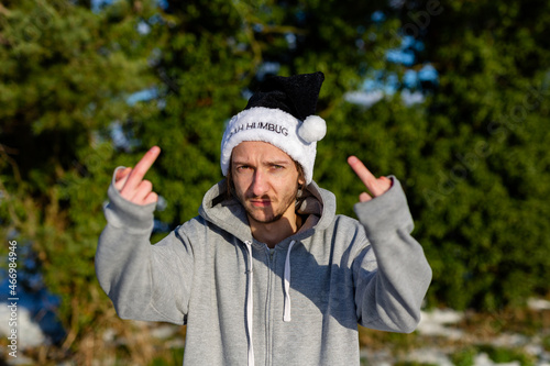 A grumpy young man wearing a black santa hat with the words Bah Humbug written on it photo