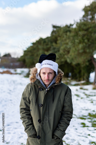 A grumpy young man wearing a black santa hat with the words Bah Humbug written on it