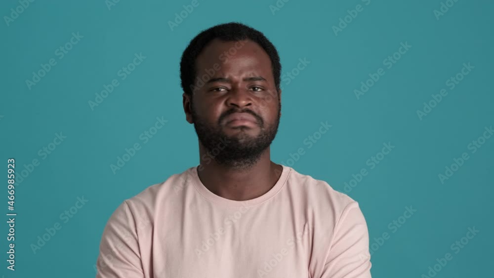 Displeased African man wearing t-shirt negatively shaking his head in blue studio Displeased African man wearing t-shirt negatively shaking his head in blue studio