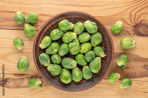 Organic ripe Brussels sprouts in a ceramic dish on a wooden table, close-up, top view.