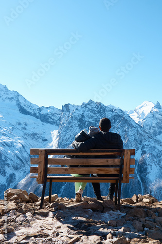 a couple of lovers are sitting on a bench in the mountains, a view from the back, rocks in the snow, a man and a woman