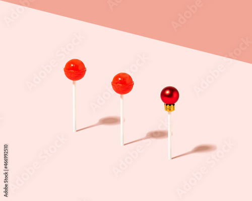 Creative composition with tasty red lollipops and Christmas bauble against pastel pink background.  Minimal xmas candy concept.