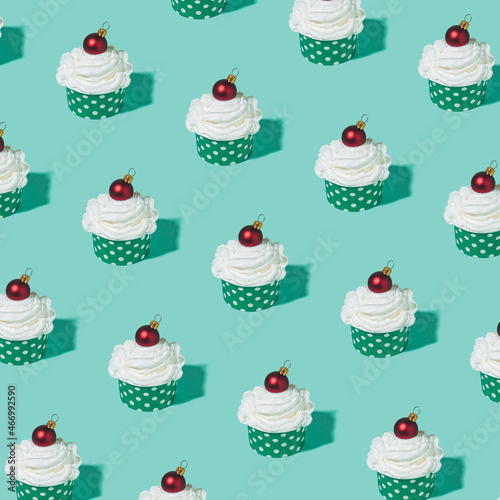 Creative pattern made of whipped cream cupcake decorated with shiny red Christmas bauble against pastel mint green background.
