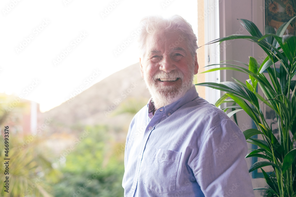 Senior bearded man standing next to the window looking at camera. Caucasian white haired elderly people Senior bearded man standing next to the window looking at camera. Caucasian white haired elderly people