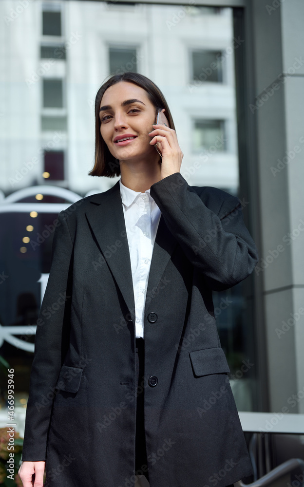 Lifestyle business portrait of attractive female freelancer, motivated young successful lady smiling looking at camera while talking on cell phone against modern corporate building background. Lifestyle business portrait of attractive female freelancer, motivated young successful lady smiling looking at camera while talking on cell phone against modern corporate building background.