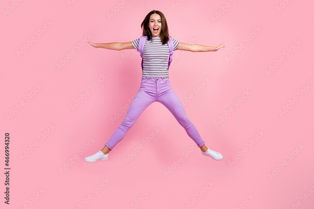 Photo of excited funky young lady wear striped outfit backpack smiling jumping high like star isolated pink color background Photo of excited funky young lady wear striped outfit backpack smiling jumping high like star isolated pink color background