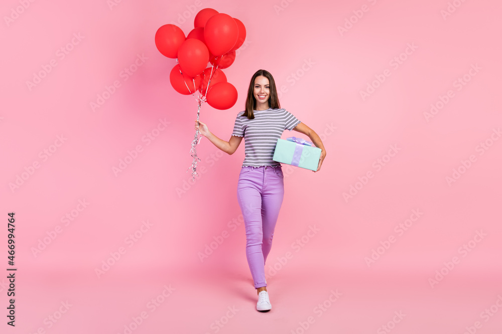 Photo of adorable shiny young woman dressed striped clothes holding many red balloons gift box smiling isolated pink color background Photo of adorable shiny young woman dressed striped clothes holding many red balloons gift box smiling isolated pink color background