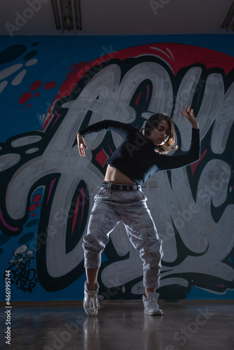 Silhouette of young woman hiphop dancer (breakdancer)dancing on graffiti studio background. Contrast colors.