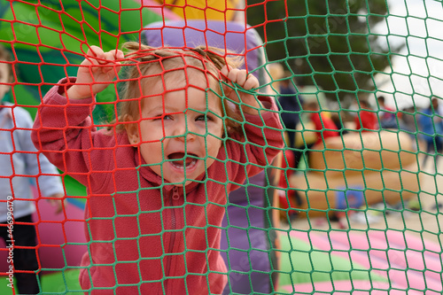 Little girl laughs as she grabs behind a playground net