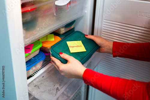 Woman placing container with frozen mixed vegetables in freezer.