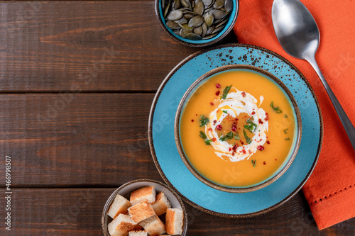  Butternut squash soup with cream, croutons, pumpkin seeds and orange napkin on one brown wooden table. Copy space. Top view