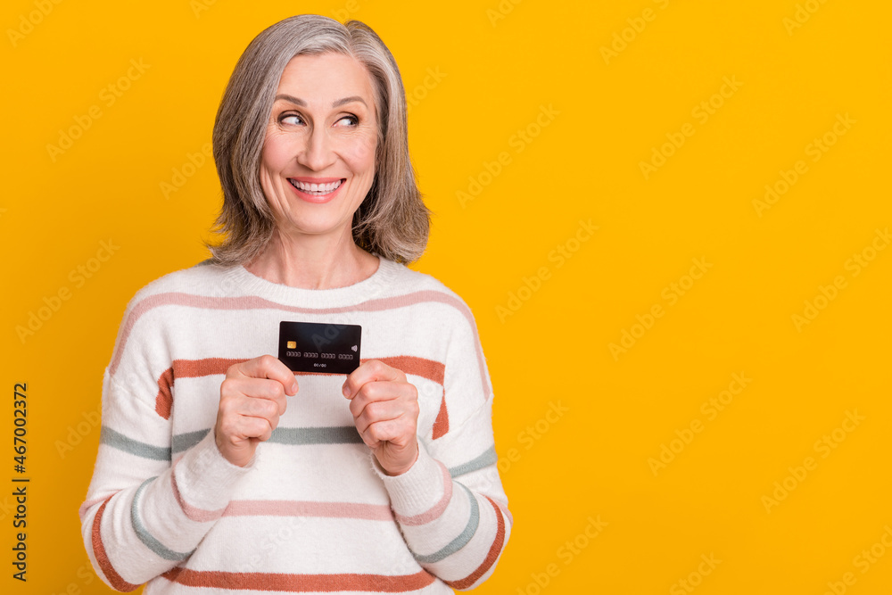 Photo of sweet charming lady pensioner wear striped pullover holding credit card looking empty space isolated yellow color background Photo of sweet charming lady pensioner wear striped pullover holding credit card looking empty space isolated yellow color background