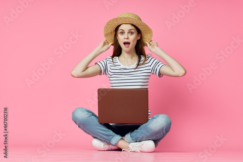 cheerful woman with laptop sitting on the floor on a pink background