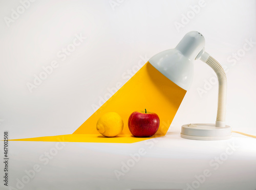 An apple and lemon under a conceptual beam of light from a table lamp