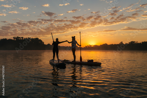 silhouettes of people on stand up paddle board with an oar and meet the rising sun