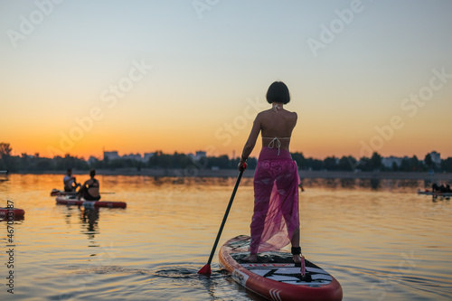 few people on stand up paddle board with an oar,  look at the rising sun