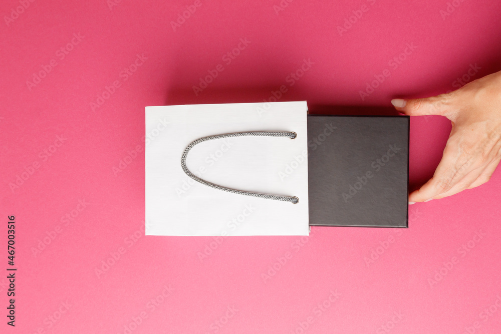 The concept of Valentine's Day. Black Friday, sale. A woman's hand takes out a small black box visible from a gift paper bag. A luxury purchase. A place to copy. Packaging for expensive gifts. Closeup The concept of Valentine's Day. Black Friday, sale. A woman's hand takes out a small black box visible from a gift paper bag. A luxury purchase. A place to copy. Packaging for expensive gifts. Closeup